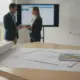 Two people reviewing fence installation plans with blueprints, a tablet, hard hat, and pencils.